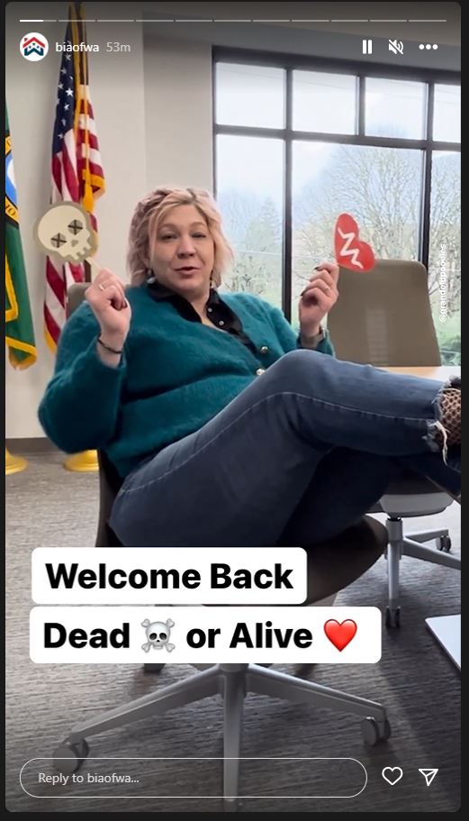 GA director Jan Himebaugh in a teal sweater and jeans with dead (skull) and alive (heart) sign