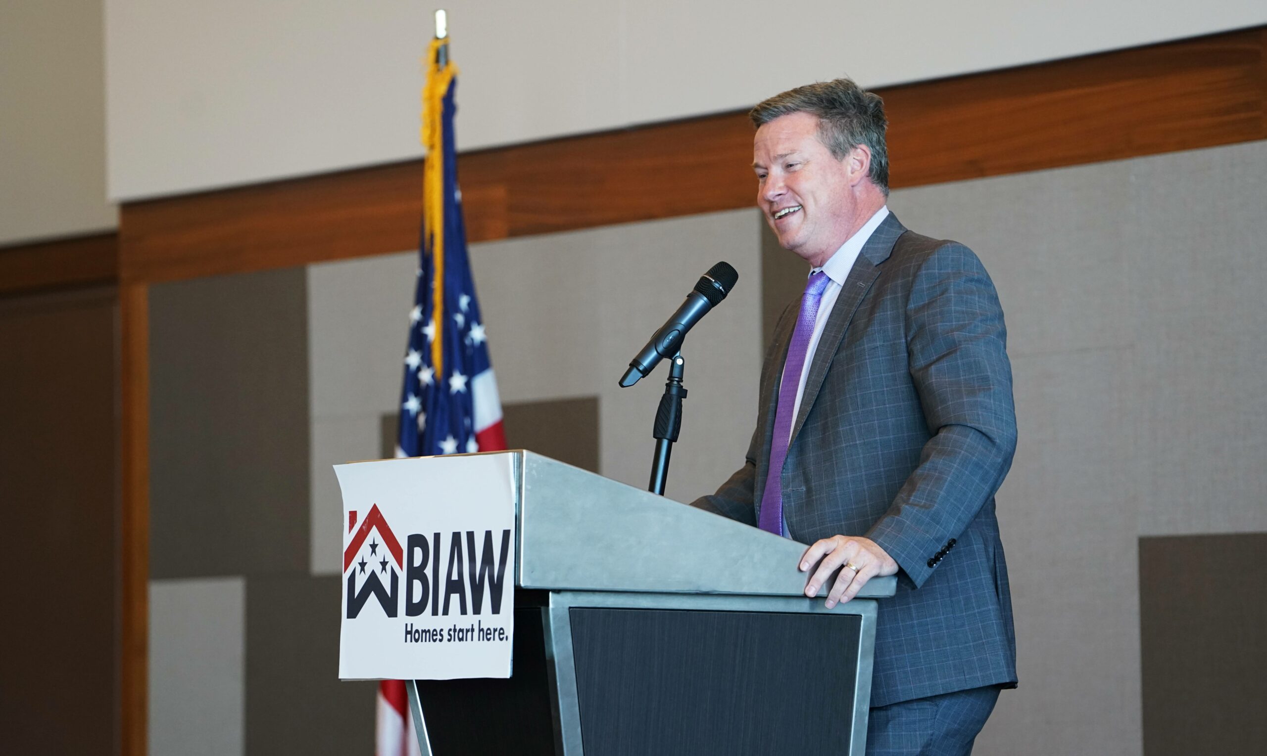 man in gray suit speaks at podium with BIAW podium sign and American flag

